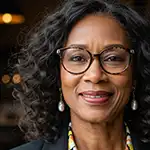 A headshot of Shanice Evans, a woman with curly hair and glasses, smiling warmly at the camera.