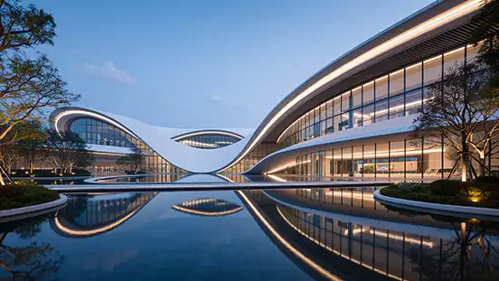 Photorealistic 3D architectural rendering of a modern, curved public building with a fluid, wave-like facade and dramatic twilight lighting reflected in a large pool.